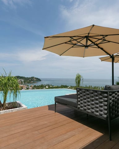 Piscina infinita en la azotea con vistas al océano, tumbonas y sombrillas sobre una terraza de madera
