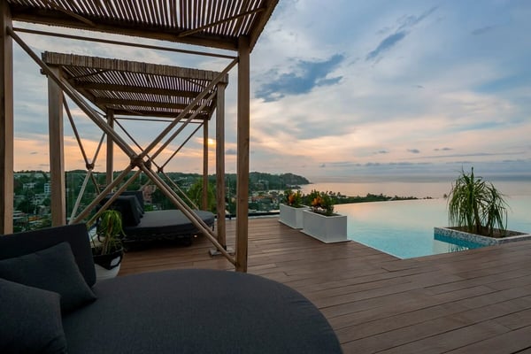 Woman in black dress standing at edge of infinity pool overlooking forested hills and valley