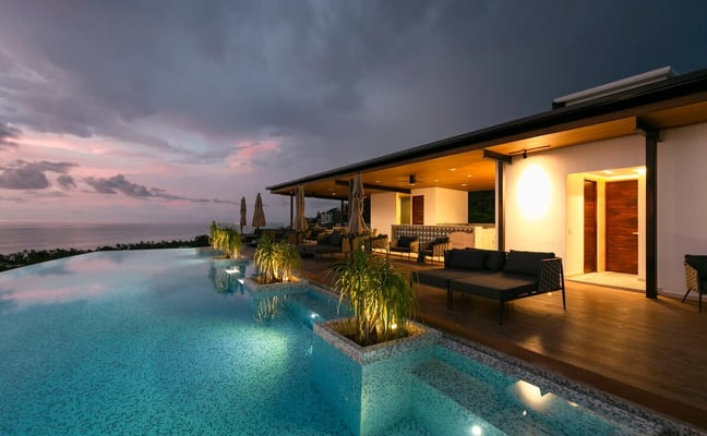 Infinity pool overlooking tropical coastline at sunset with dramatic cloudy sky and palm plants